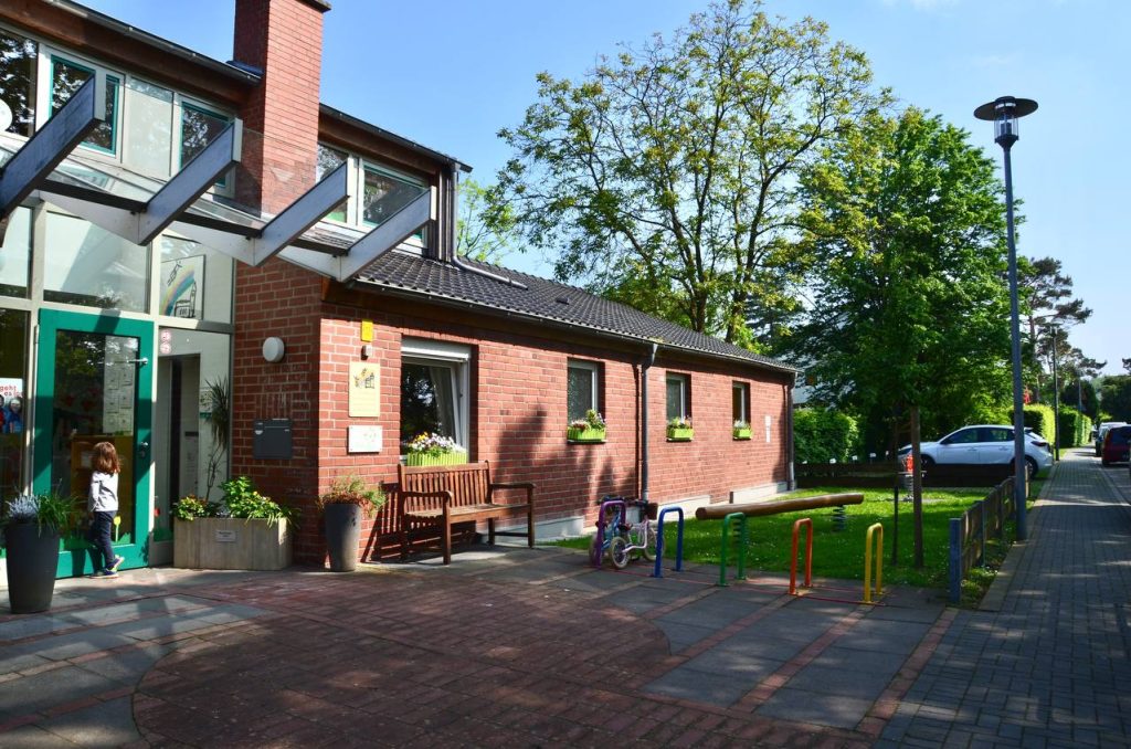Front entrance of a Montessori kindergarten in Düsseldorf with brick exterior, green door, and outdoor seating area