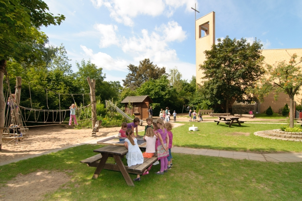 Children playing in the outdoor area of a Montessori kindergarten Düsseldorf with rope bridge, playground, and church building in the background