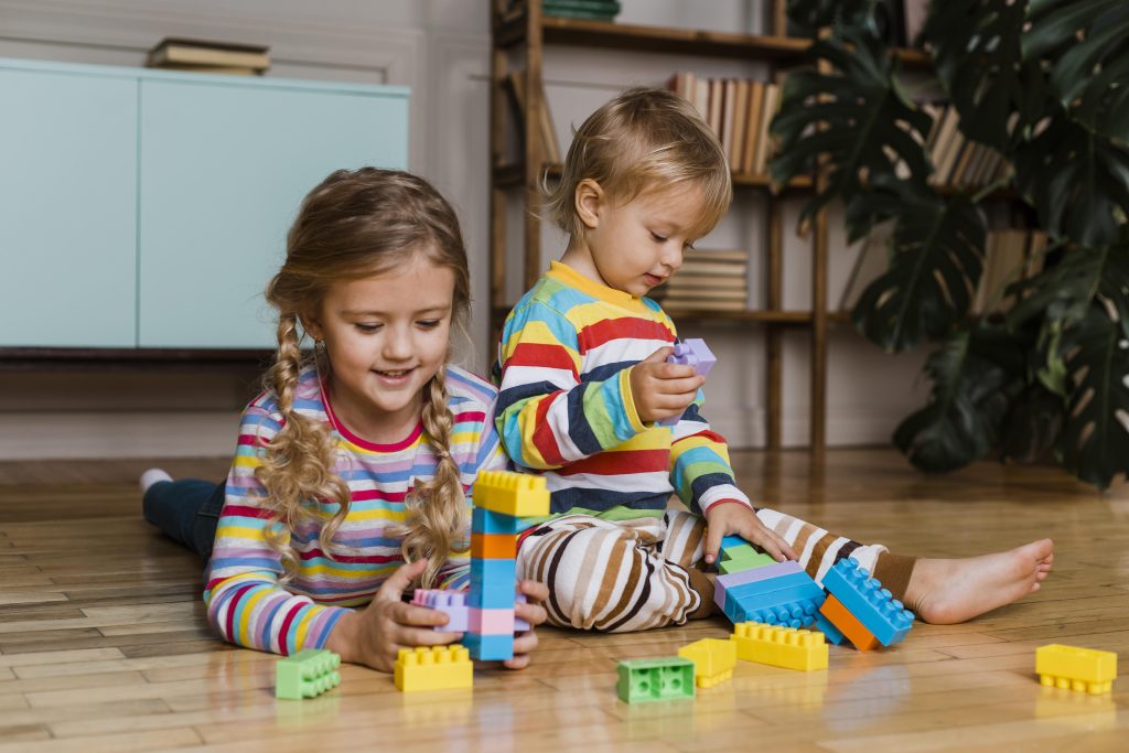 Two young children in colorful striped clothes playing with building blocks on the floor at home.