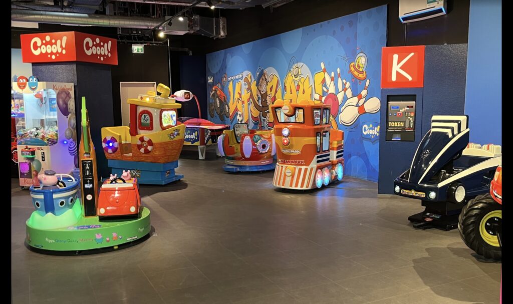 Indoor arcade area for kids with coin-operated rides, colorful mini vehicles, and animated wall art in a family entertainment center