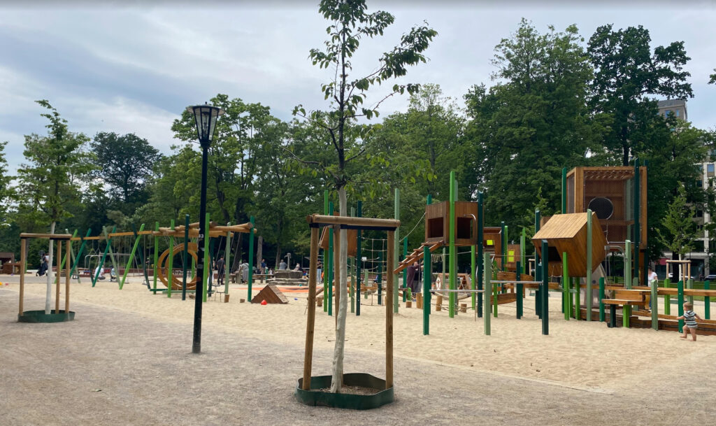 Spielplatz im Hofgarten – Large modern outdoor playground in Düsseldorf with wooden climbing towers and swings surrounded by trees