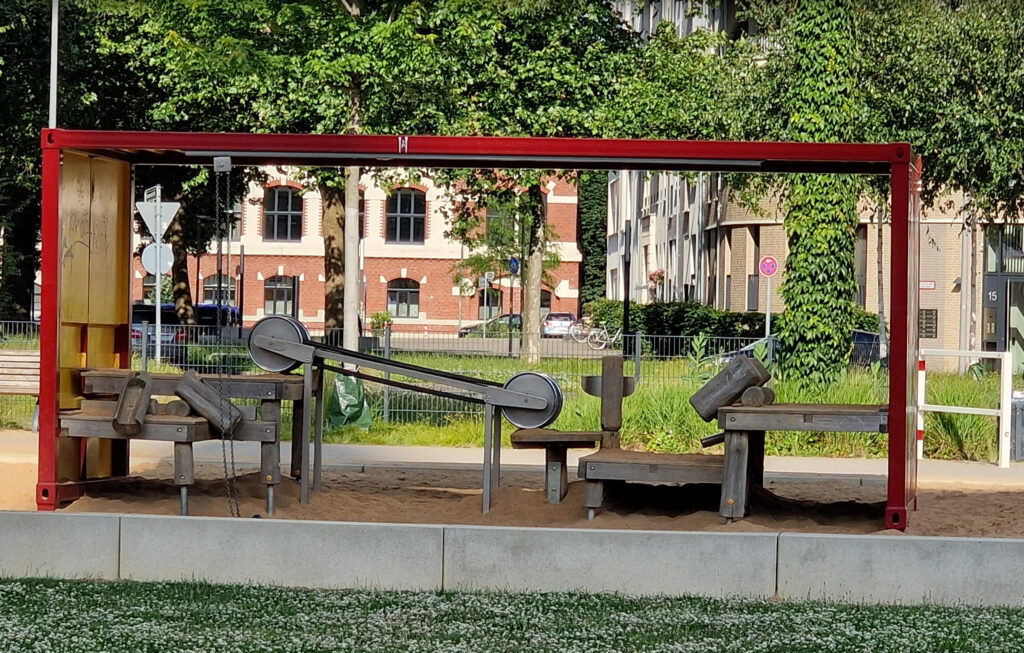 Stadt-Natur-Park Flingern – Wooden seesaws and benches under a red frame at a modern outdoor playground in Düsseldorf