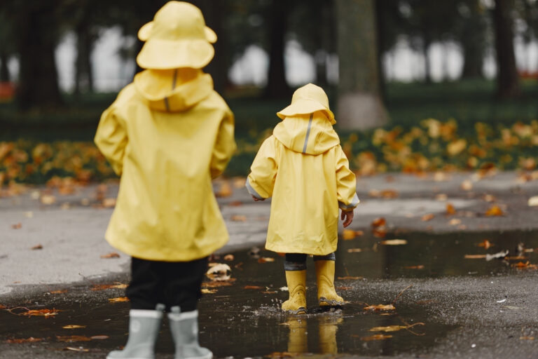 Children in yellow raincoats playing in puddles on a rainy autumn day in Düsseldorf — a reminder of the need for indoor activities in Düsseldorf for kids