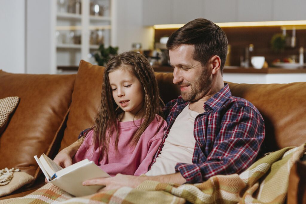 Father and daughter sitting at a couch and reading