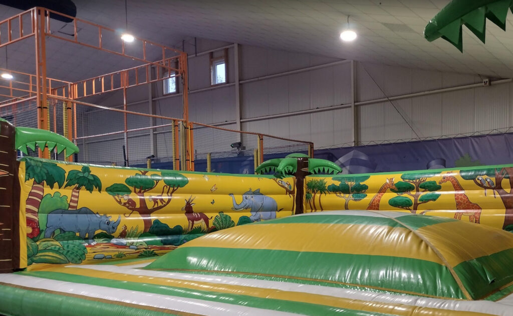 Jungle-themed inflatable bounce zone with animal illustrations and soft play structures for kids