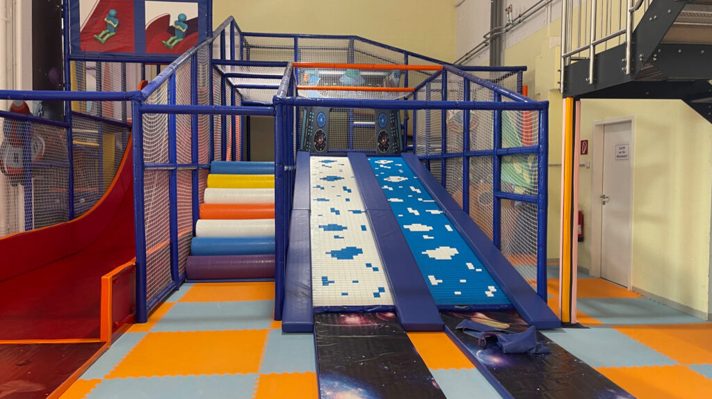 A space-themed slide, climbing obstacles, and colorful padded flooring for young children