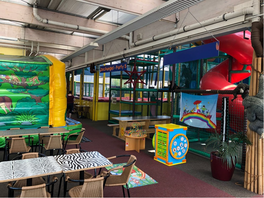 Indoor playground in NRW with jungle-themed bounce house, red tube slide, party area, and toddler activity stations