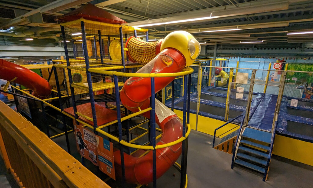 Indoor playground in NRW with spiral tube slide, rope tunnel, and trampoline area for active children