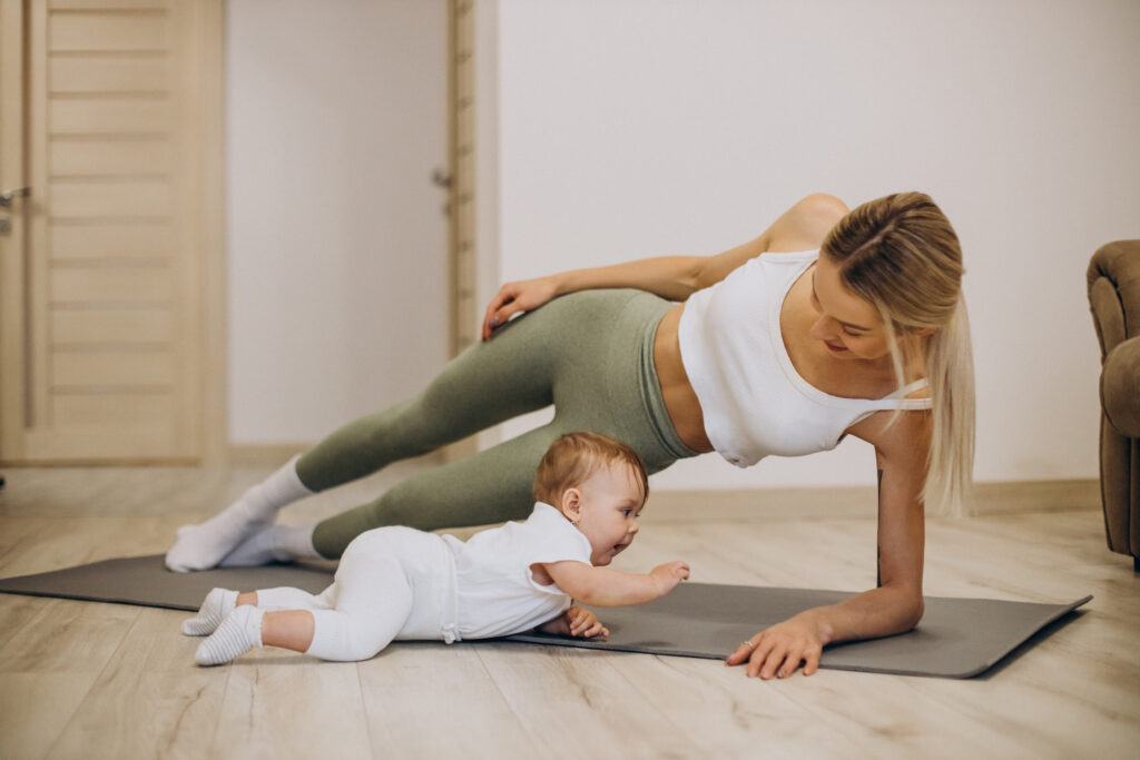 Mother practicing side plank yoga pose on a mat while her baby plays next to her during a family yoga session in Düsseldorf