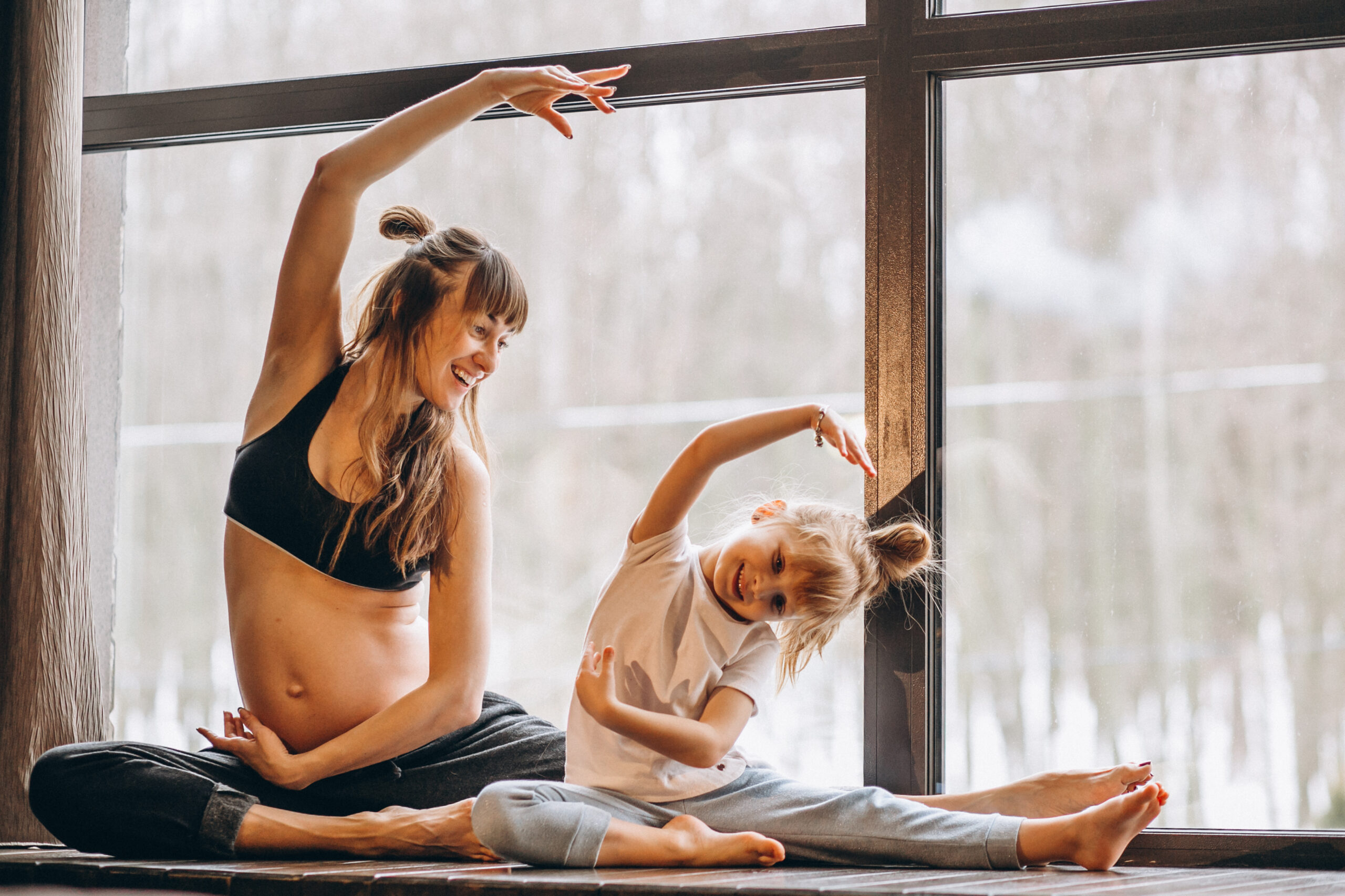 Pregnant woman and young daughter smiling and stretching together during a kids yoga class in Düsseldorf.