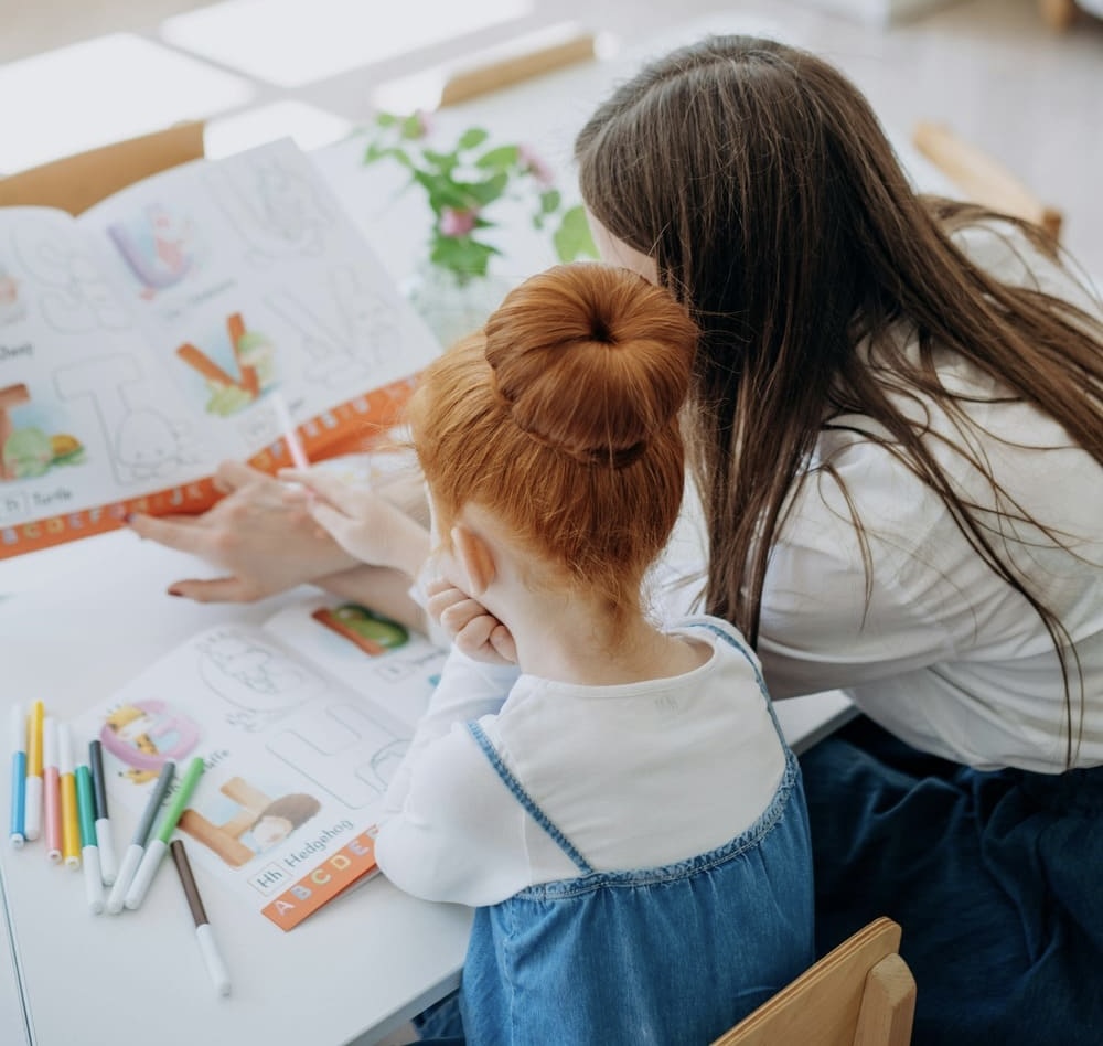 Adult guiding a child through hands-on Montessori literacy activities using illustrated worksheets and letter sounds
