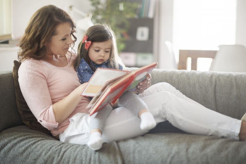 Eltern, die zu Hause mit einem Kleinkind ein Bilderbuch lesen, um durch gemeinsames Lesen und sprachliche Bindung die frühe Lesefähigkeit zu fördern