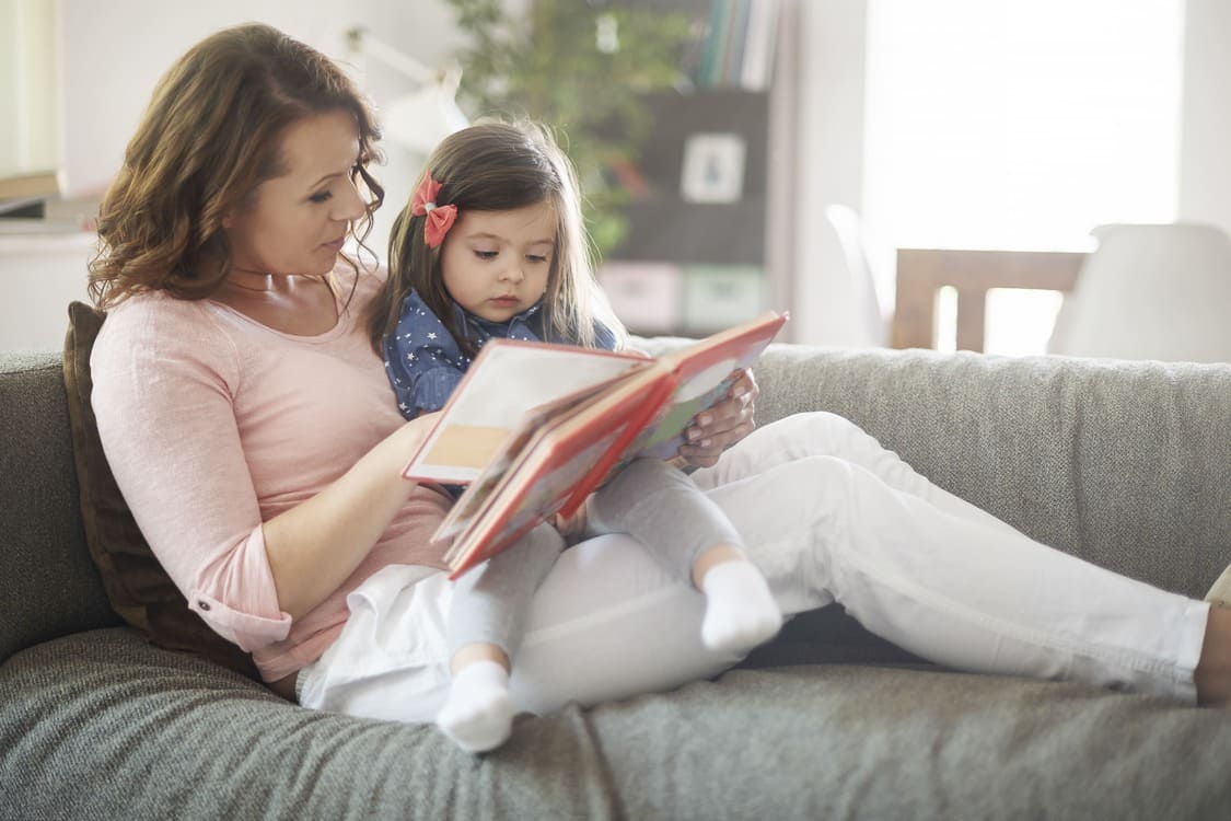 Parent reading a picture book with a young child at home, supporting early literacy through shared reading and language bonding