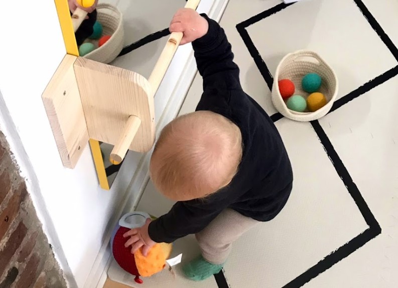 Baby engaged with physical toys and a wall mirror, highlighting sensory-rich play over touchscreen interactions
