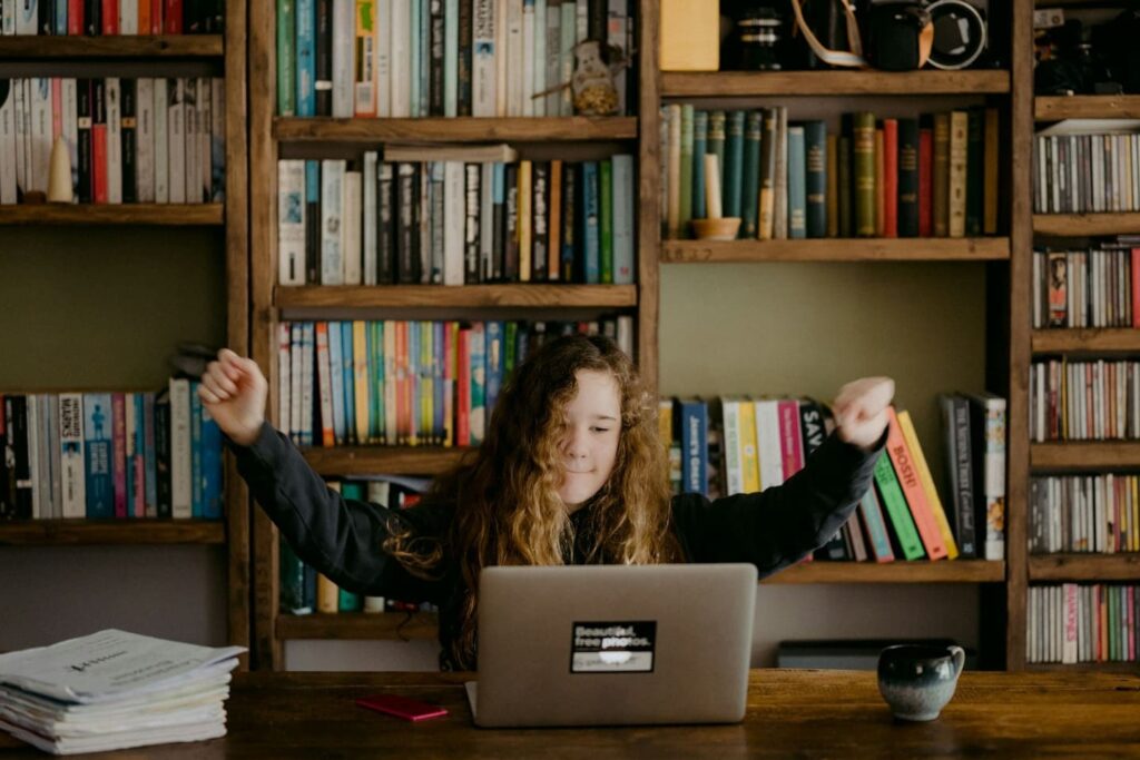 Girl learning coding on a laptop in a book-filled Montessori-style home environment—representing balanced, independent learning in Montessori coding for children.