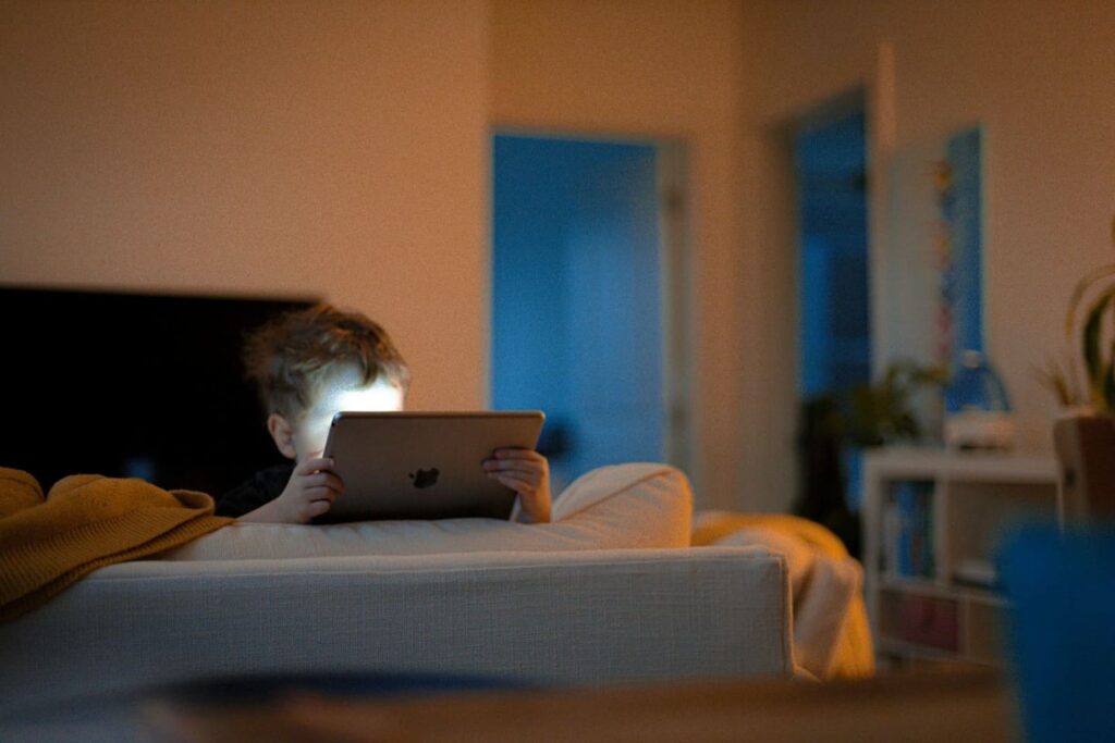 Child staring at a tablet in a dimly lit room — illustrating the downsides of excessive screentime in early coding education for children.

