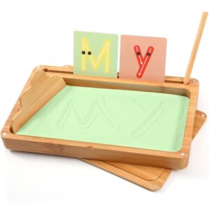 Montessori tracing tray with green sand and guide cards for letter formation, offering a multisensory writing activity that strengthens fine motor control and phonetic awareness.

