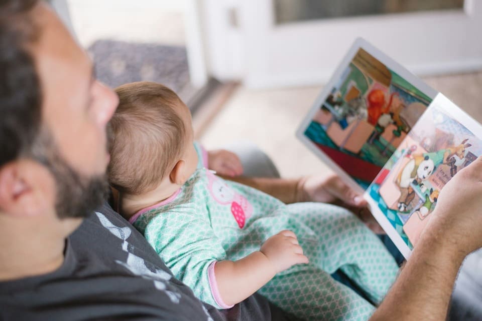 Parent reading a picture book to an infant, showing how the Montessori method introduces language and reading through spoken word and visual exposure from birth.

