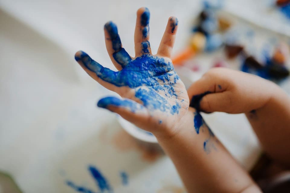 Child’s hand covered in blue paint during a sensory activity, demonstrating Montessori-inspired hands-on learning that supports early writing development and prepares for reading.

