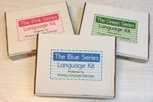 Montessori language kit boxes labeled Pink, Blue, and Green Series representing the phonics-based reading progression used in Montessori literacy education.

