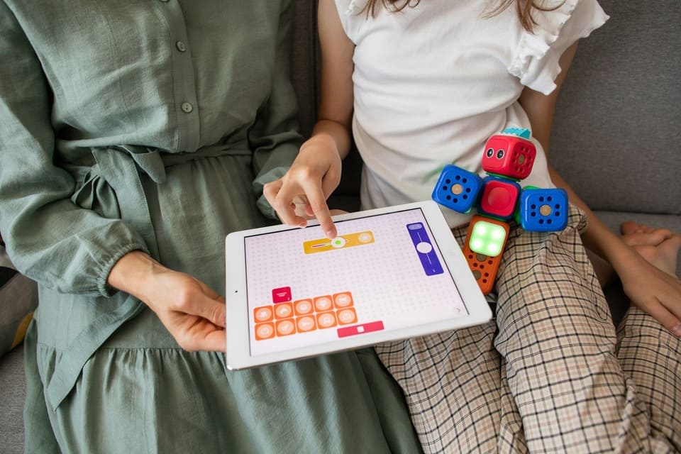 Montessori student and teacher using a tablet and coding blocks to explore Montessori AI learning tools, combining hands-on play with digital interaction.