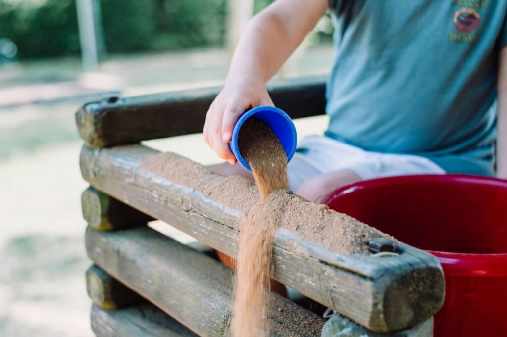Child pouring sand during a sensory activity outdoors — showcasing Montessori hands-on learning for children with ADHD.