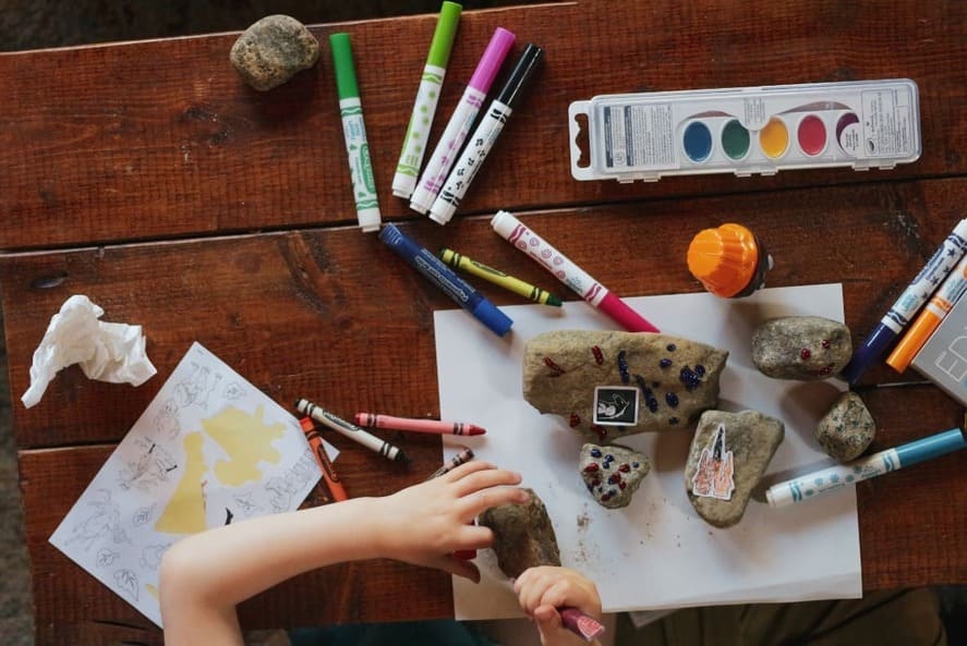 Montessori art setup with stones, markers, and paints on a wooden table, encouraging open-ended creativity in a prepared environment.