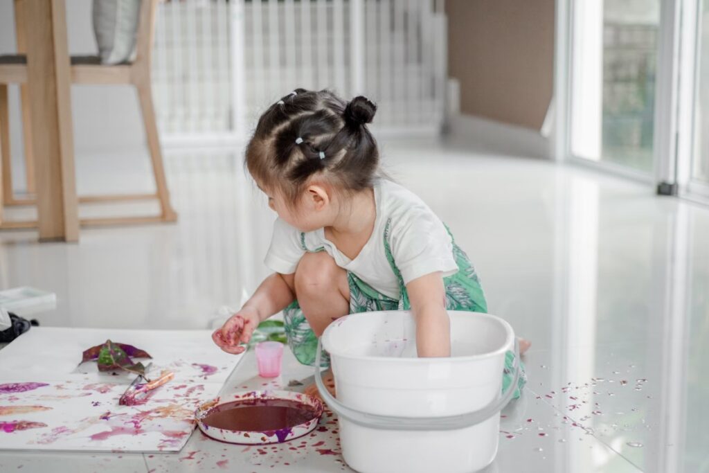 Toddler exploring a messy Montessori art station with paint and water, experiencing freedom of expression in a self-directed creative space.