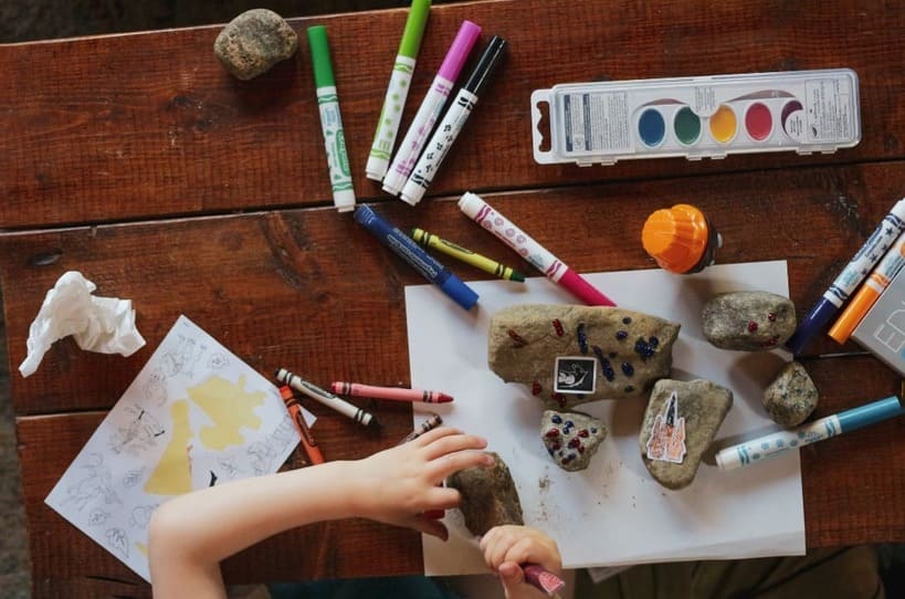 Child creating art with rocks, crayons, and markers — a hands-on Montessori at home activity that supports independence and creativity.

