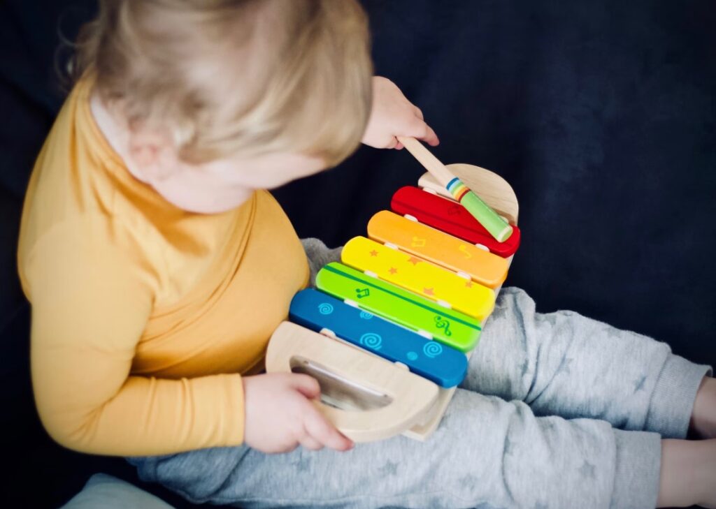 Child playing a wooden xylophone, developing fine motor skills and pitch recognition.