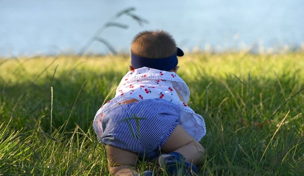 Baby crawling on grass near a lake during a Montessori child-led walk, representing early outdoor exploration and sensory development in nature-based Montessori activities.

