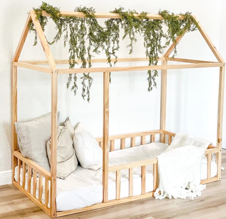 Natural wood Montessori floor bed with pillows and greenery, ideal for promoting child-led sleep and independent movement
