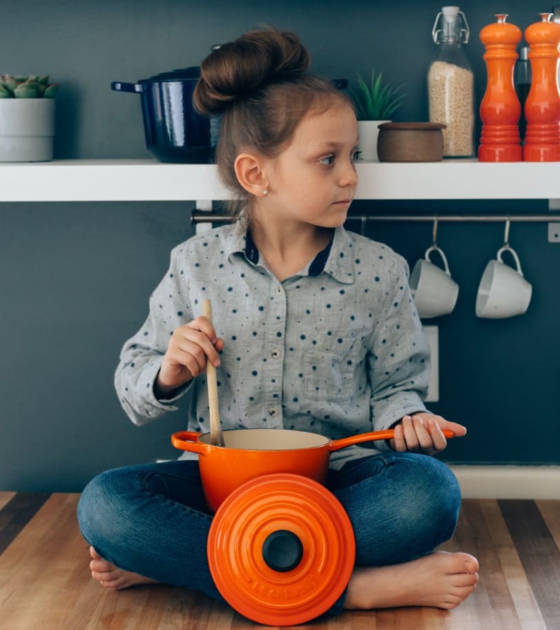 Young child using a wooden Montessori play kitchen to engage in imaginative food preparation, supporting early practical life skills through realistic role play.

