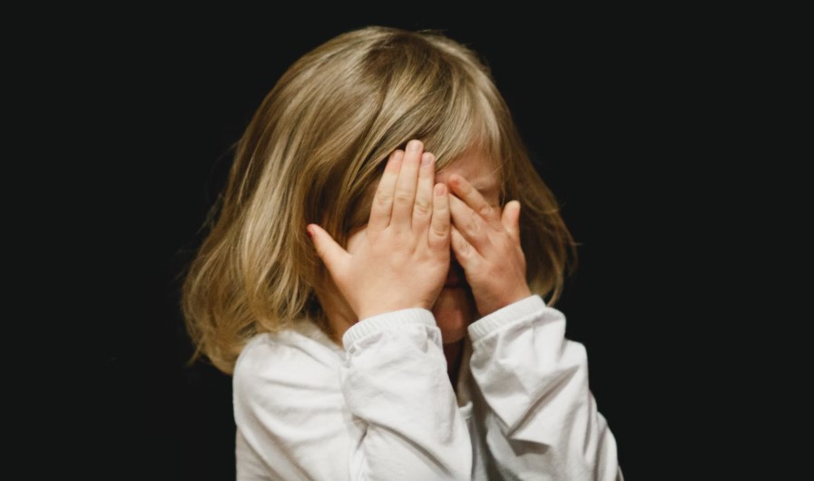 A young child covering their face in a moment of frustration — illustrating the challenges some autistic children may face in less structured Montessori environments.