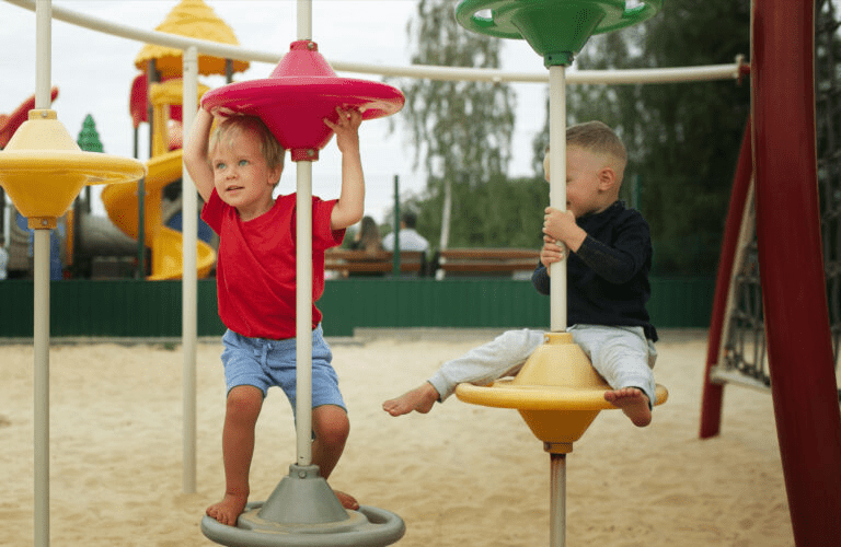 Two boys playing on spinning poles at an outdoor playground