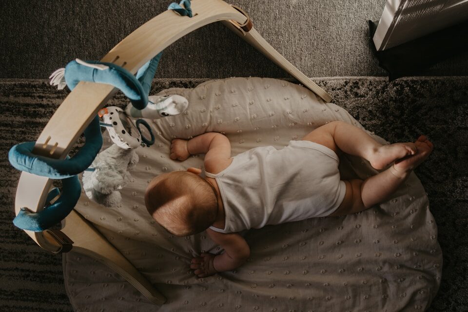 Baby practicing early floor time under a play gym — how to help baby crawl through safe exploration.