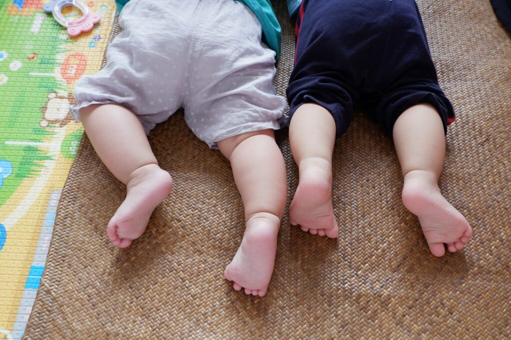 Two babies lying side by side on a play mat during early movement exploration.