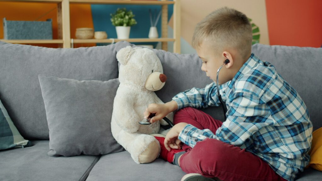 Ein Kind benutzt ein Spielzeugstethoskop, um einen Teddybären zu "untersuchen" - ein klares Beispiel für symbolisches Spiel, das vorgetäuschtes Spiel, Rollenübernahme und reale Routinen miteinander verbindet.