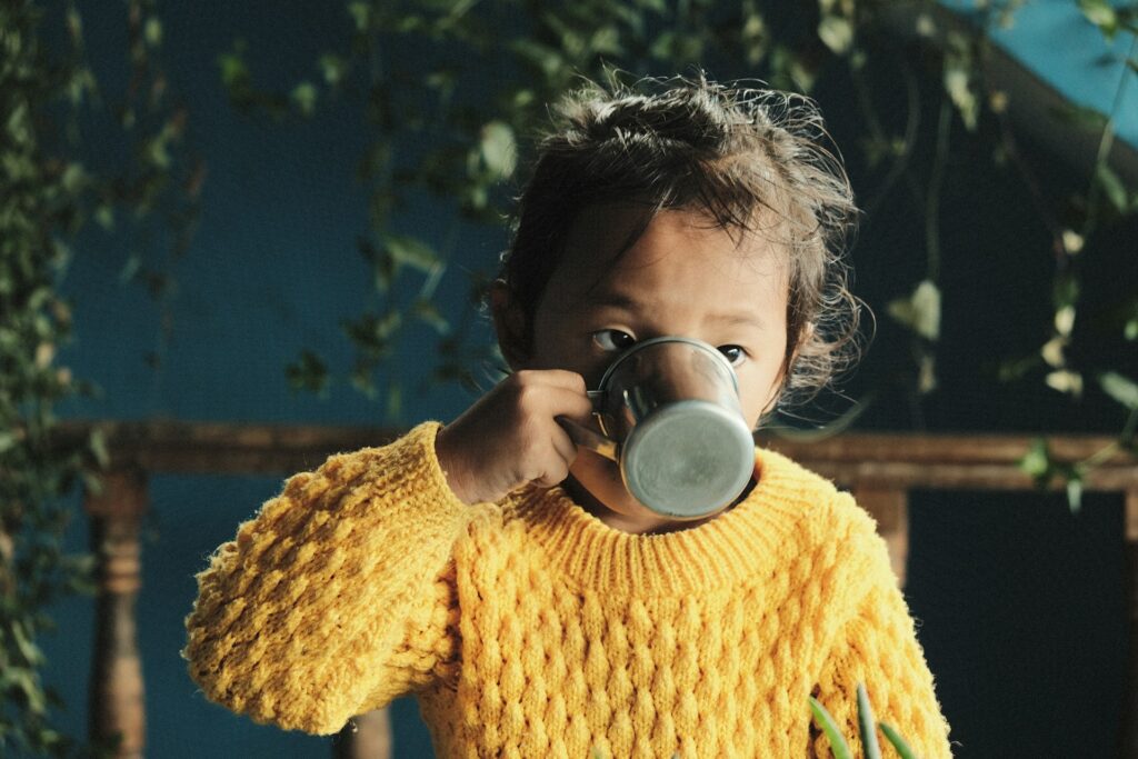 Child lifting a cup as if sipping tea — symbolic play that suggests imagined content and “as if” actions, even when the story is not physically visible.