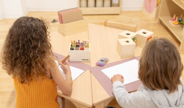 Children working side by side in a bilingual Montessori environment using art and writing materials, encouraging concentration, collaboration, and language-rich activities in a prepared learning environment.